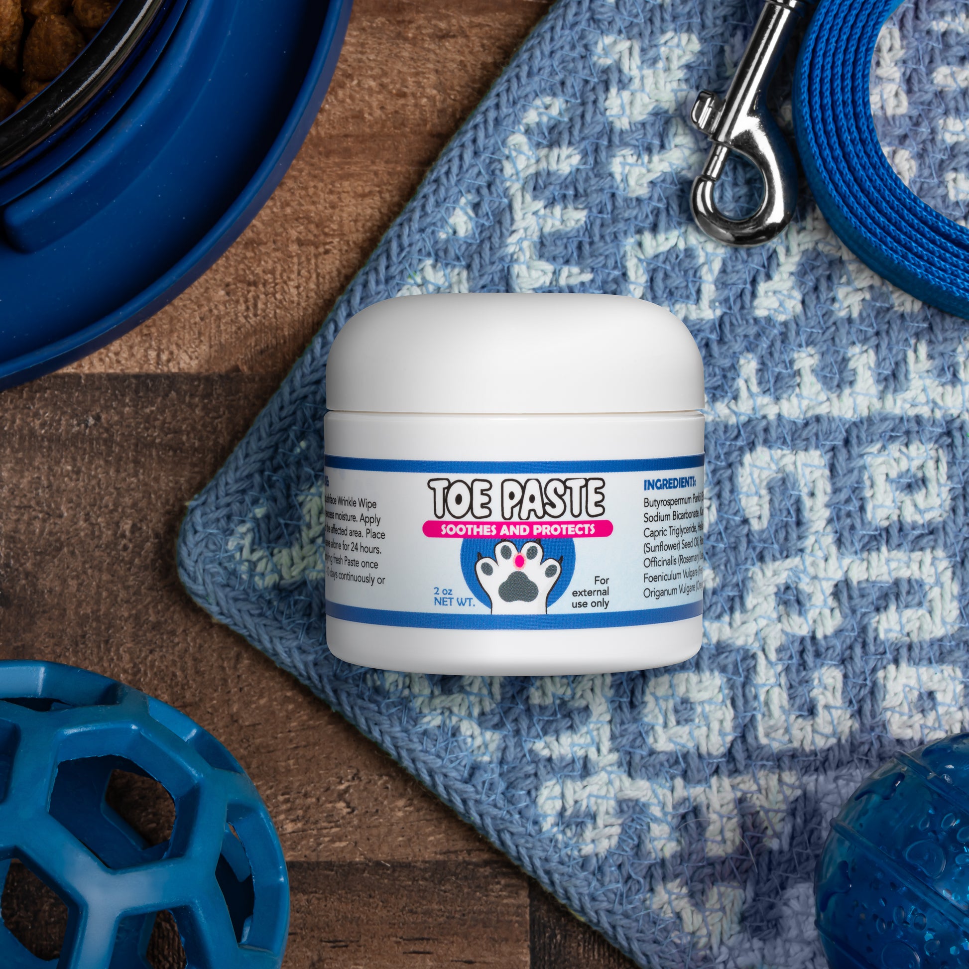 Jar of toe paste for pets on a textured surface with pet accessories.