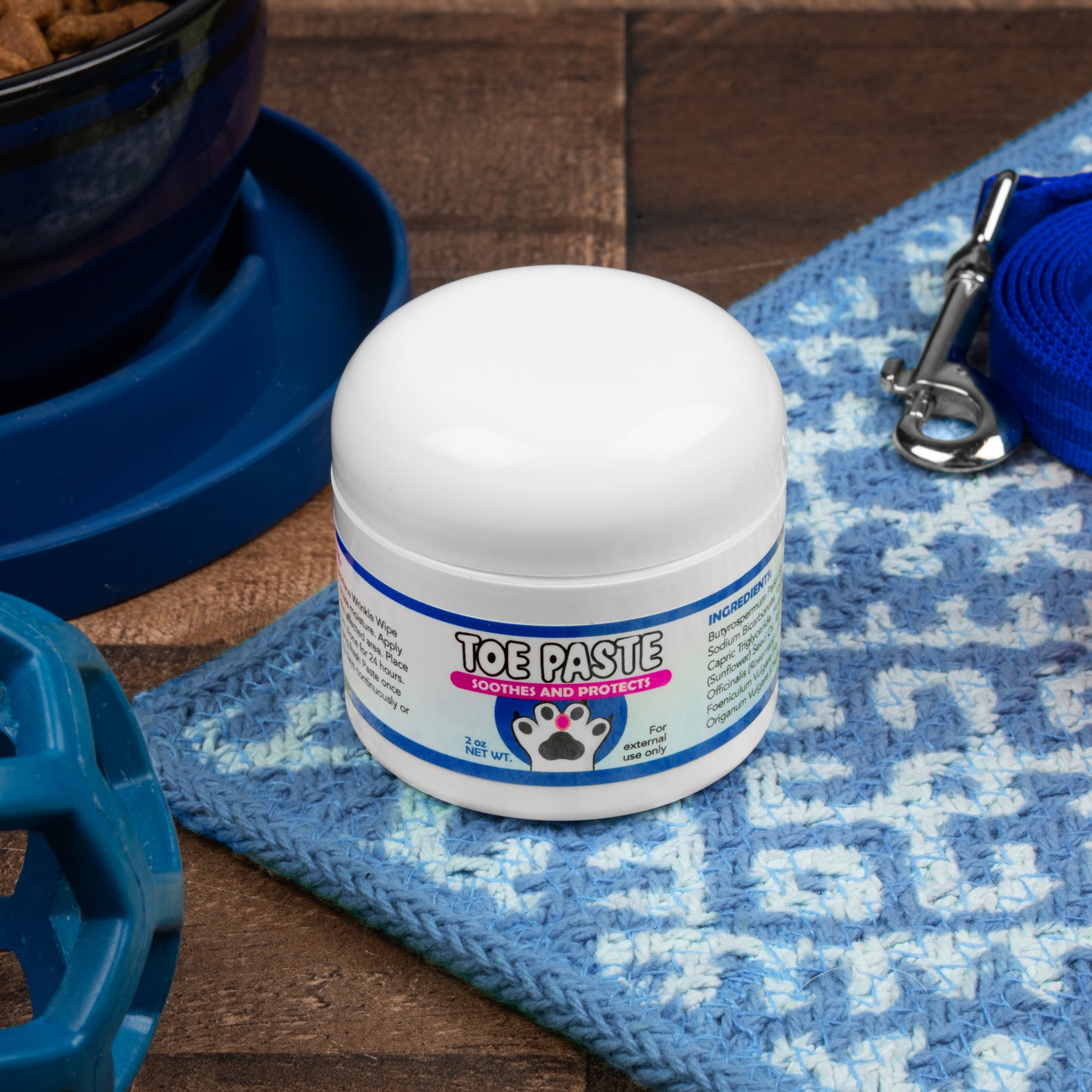 Jar of toe paste for pets on a blue mat with pet accessories.